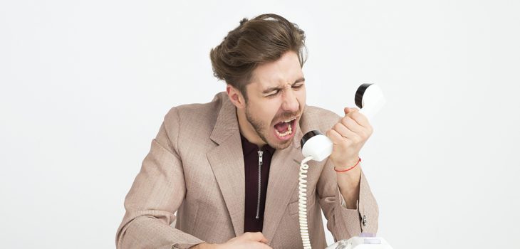 Brown haired man in a suit yells into a rotary phone